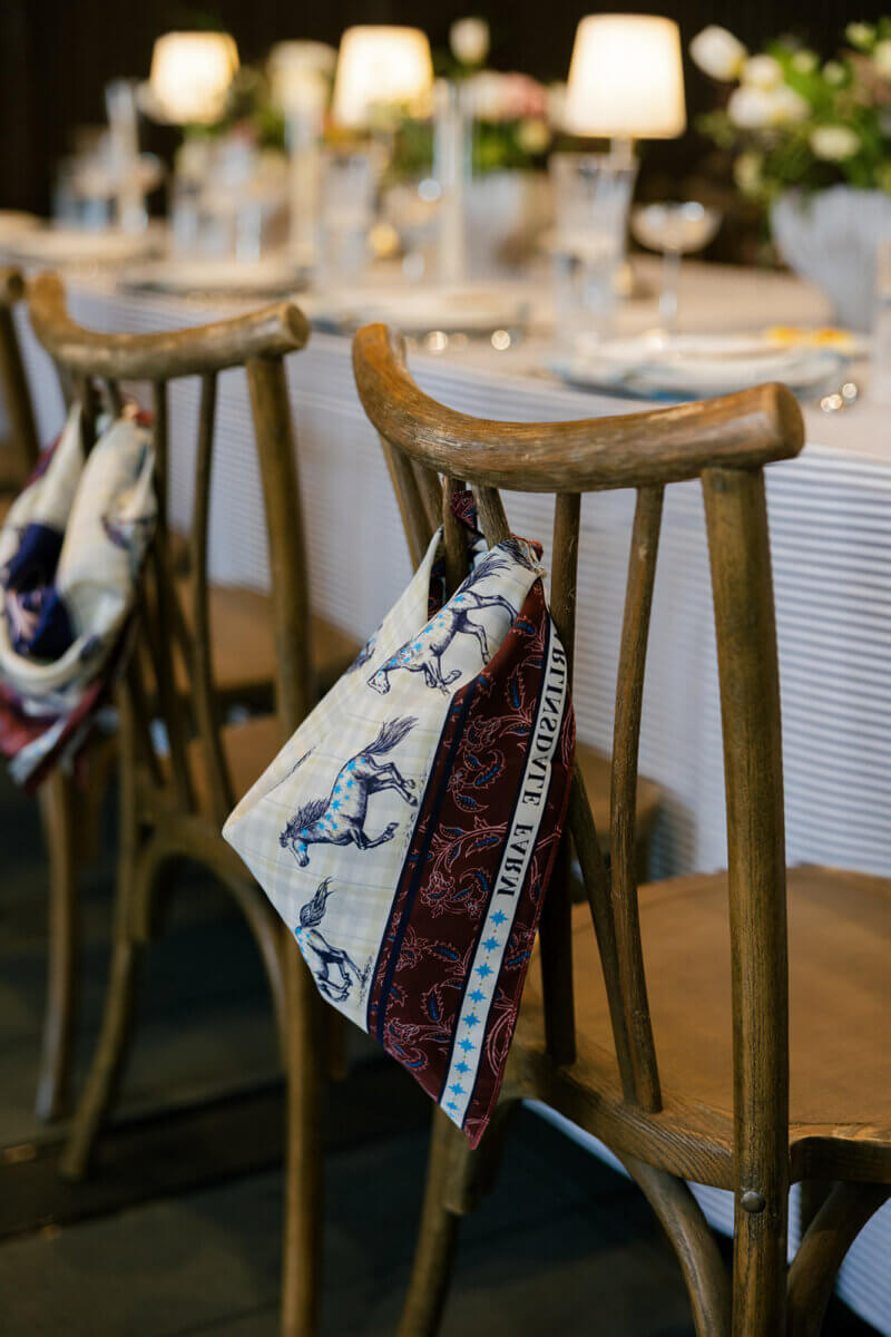 This Dreamy Equestrian Wedding Made History at Franklin's Harlinsdale Farm - 12 A wooden chair at a set dining table at Harlinsdale Farm in Franklin has a patterned scarf with horses draped over the backrest, adding rustic elegance to this charming wedding scene.