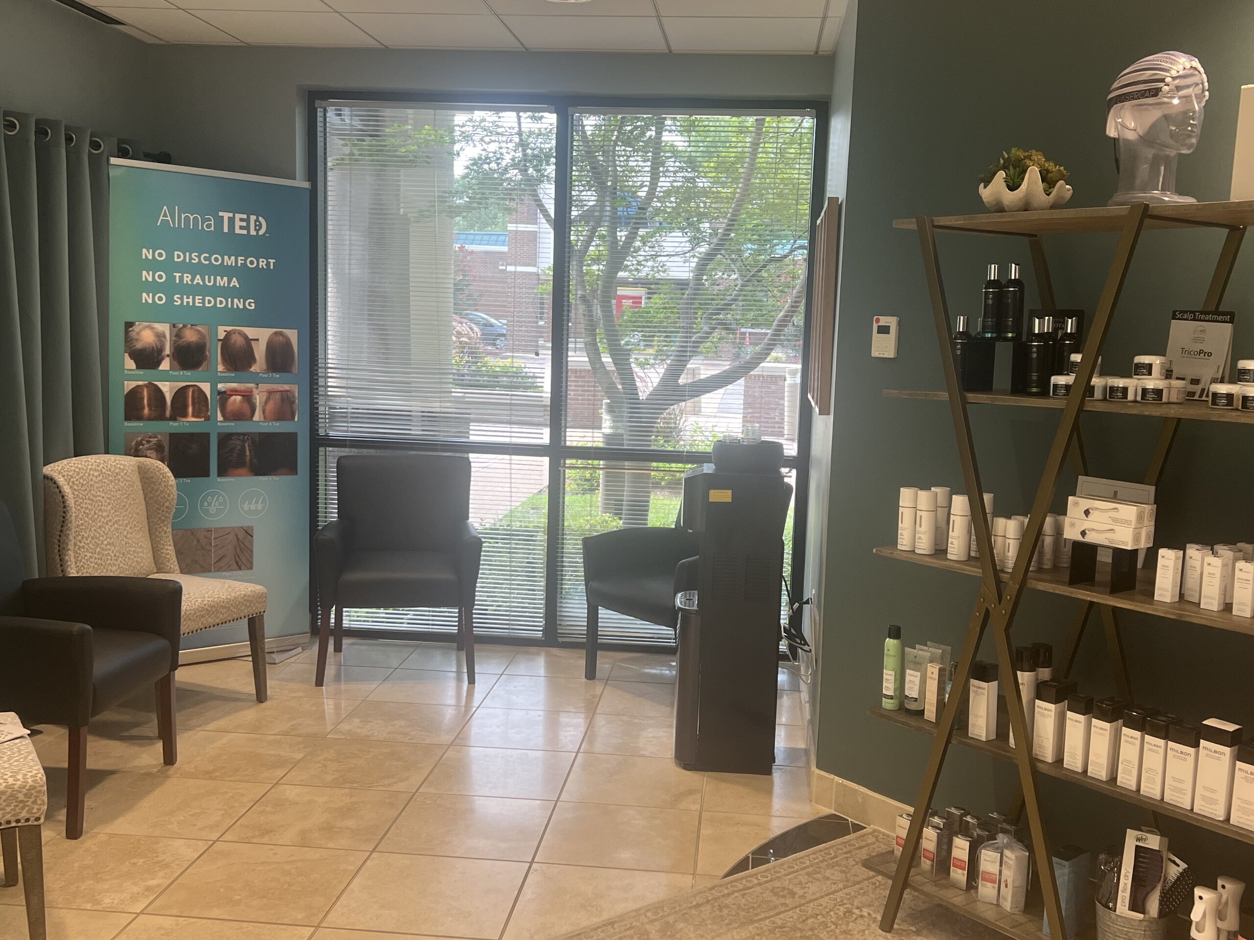 A welcoming waiting area with chairs, a display shelf holding hair products, a window with blinds, and signage advertising Alma TED for hair treatment—reflecting the professional atmosphere of HPIHair Partners, a trusted hair clinic specializing in advanced hair restoration solutions.