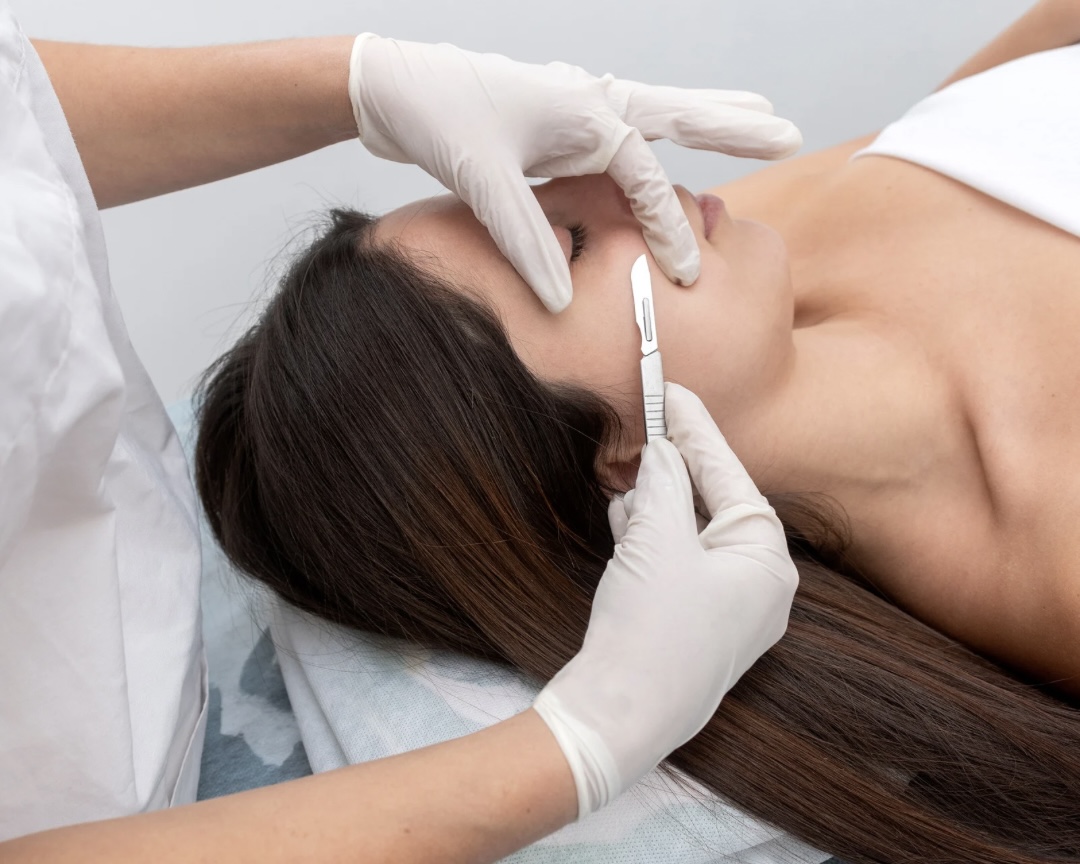 Nashville Steals, Deals & Announcements: July 2026 - 4 A person lying down with eyes closed receives a facial dermaplaning treatment from a professional wearing white gloves and holding a small blade, enjoying exclusive July deals on this rejuvenating service.