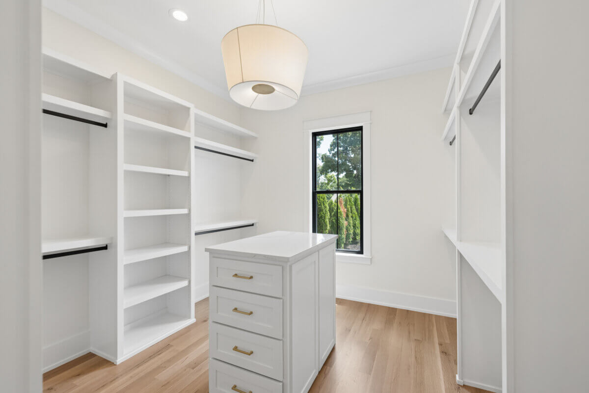 A Look Inside Brentwood's Newest Luxury Address - 10 Spacious walk-in closet with white shelves, hanging rods, a center island with drawers, wood flooring, and a window letting in natural light.