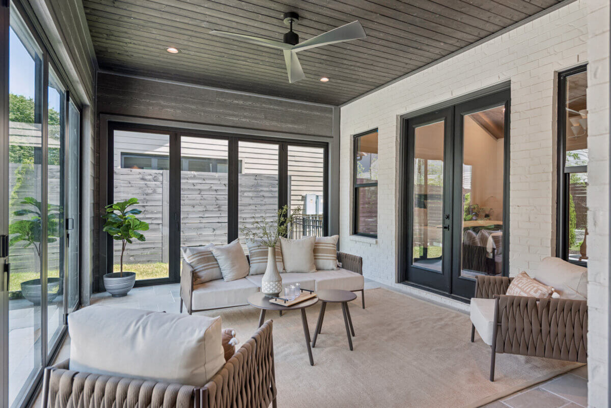 A Look Inside Brentwood's Newest Luxury Address - 7 Modern sunroom with large windows, light furniture, potted plants, a ceiling fan, and neutral colors creates a sense of luxury while offering a serene view of the fenced backyard—perfect for enjoying the ambiance of Brentwood’s newest address.