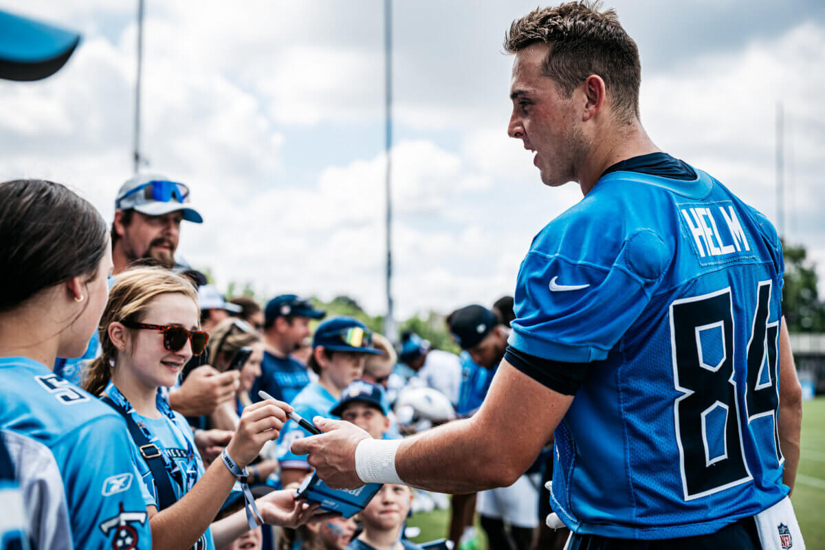 Football player in a blue jersey signs autographs for fans, including a girl with sunglasses, at an outdoor Tennessee Titans event highlighting their Youth Programs and memorable Kids Experiences.