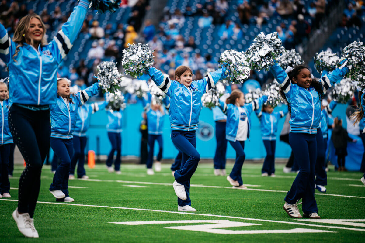 Titans cheerleaders perform with young girls at a Titans game.