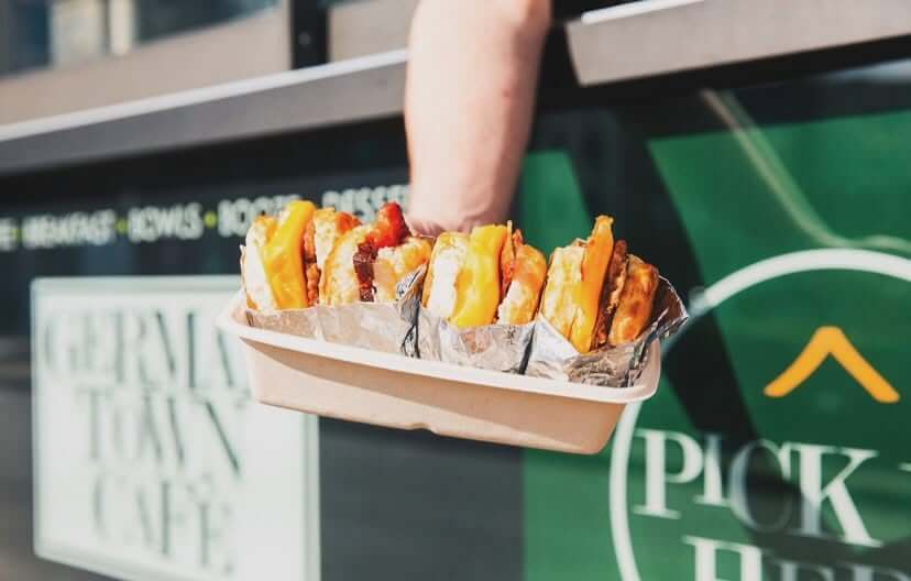 11 Walk-Up Windows To Try in Nashville - 3 A person holds a takeout container filled with several cheeseburgers, seen outdoors in front of a green sign and a windowβcapturing the classic charm of Nashvilleβs popular walk-up windows.