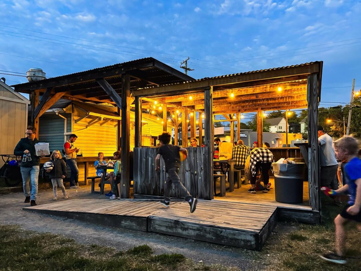 11 Walk-Up Windows To Try in Nashville - 5 People are dining and socializing under a lit wooden pavilion at dusk, while children play and run in the foreground outside the structureβcapturing the vibrant energy inspired by popular walk-up windows in Nashville.