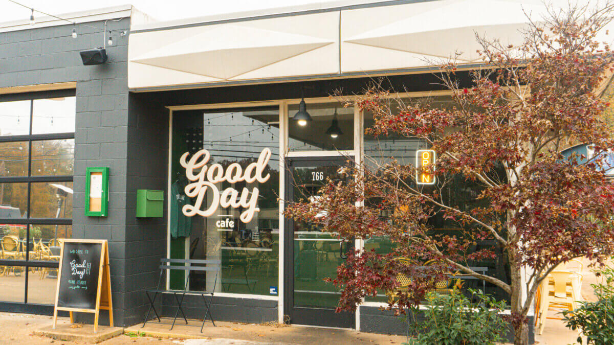 An Ode to Oxford: How to Eat Your Way Through This Delicious Small Town - 9 Exterior of Good Day Cafe, one of the standout Oxford restaurants, with large window signage, a neon "OPEN" sign, a menu board on the sidewalk, and a tree with reddish leaves in front.