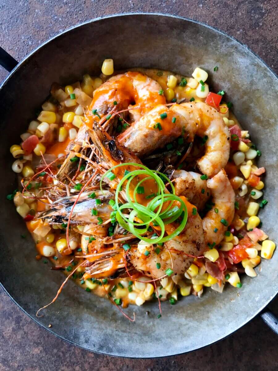 An Ode to Oxford: How to Eat Your Way Through This Delicious Small Town - 13 Grilled shrimp served on a bed of corn, diced tomatoes, and chives, garnished with a spiral of green onion in a metal dish—a vibrant example of fresh cuisine reminiscent of the culinary artistry found in top Oxford restaurants.