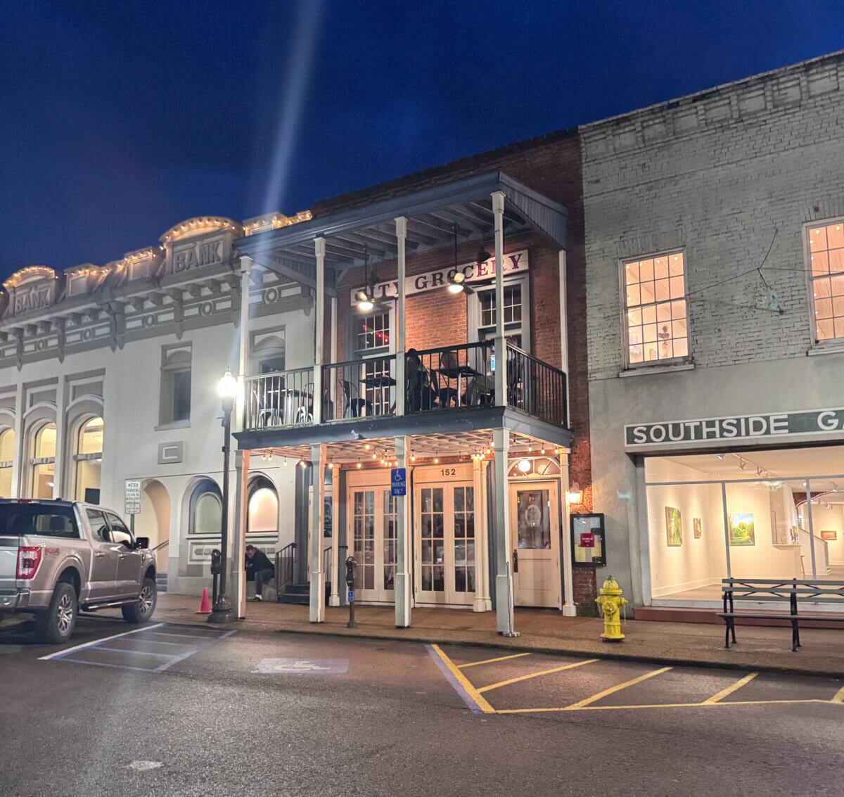 An Ode to Oxford: How to Eat Your Way Through This Delicious Small Town - 6 Street view of a historic building at night with a two-story porch, lit windows, a parked truck, and a yellow fire hydrant in front.