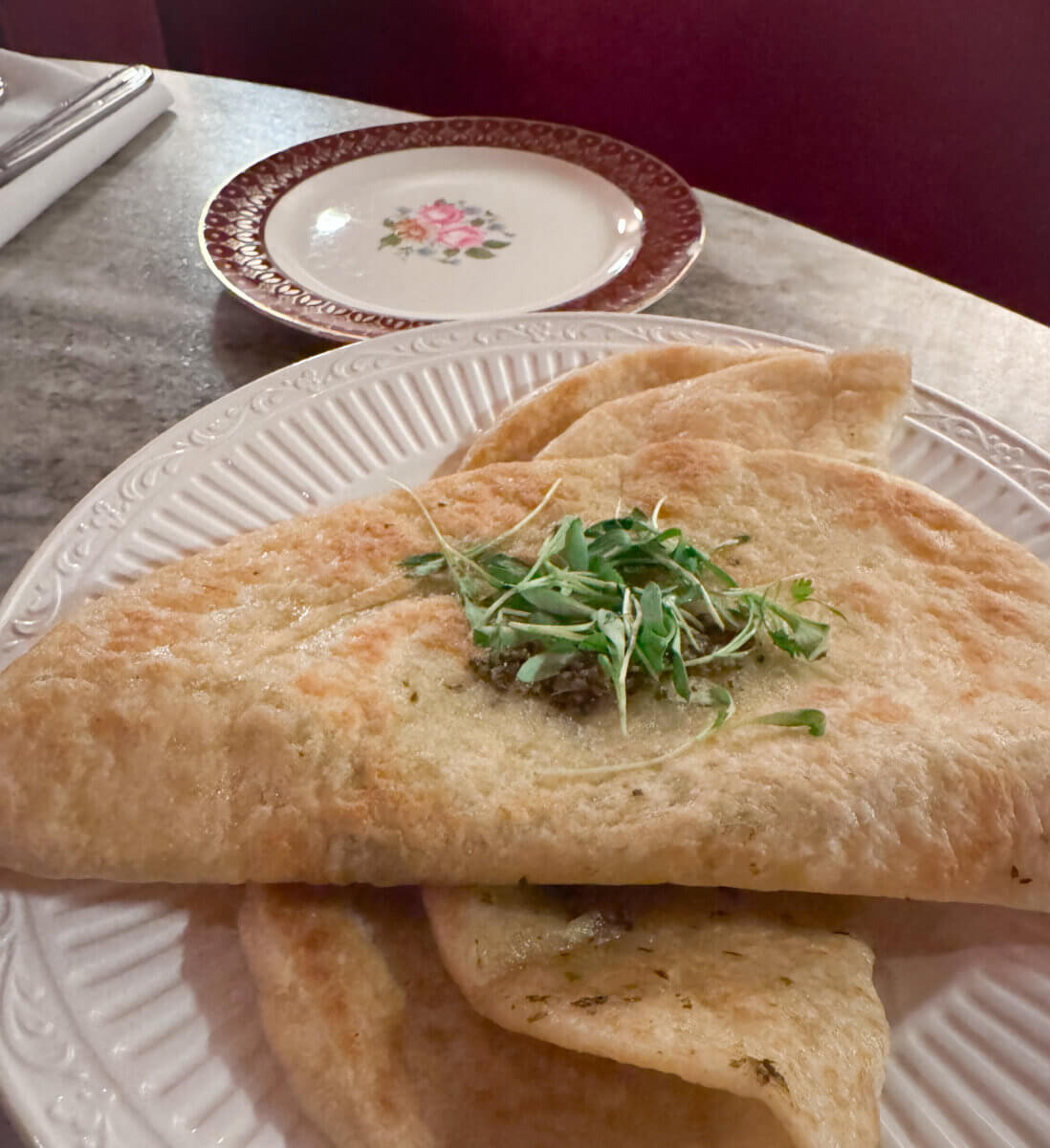 An Ode to Oxford: How to Eat Your Way Through This Delicious Small Town - 12 A folded flatbread topped with microgreens is served on a white plate, with a decorative floral saucer in the background on a marble table.