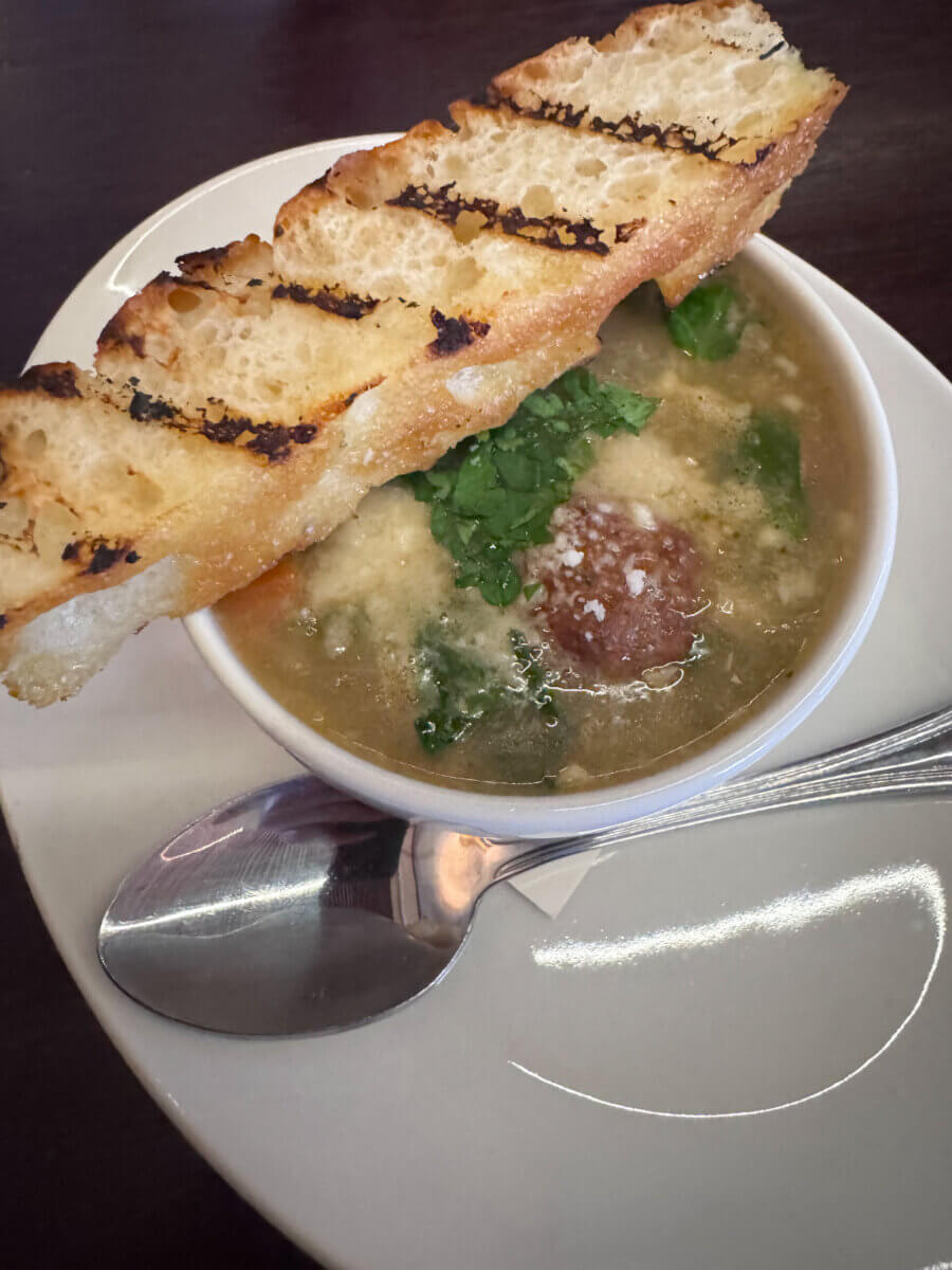 An Ode to Oxford: How to Eat Your Way Through This Delicious Small Town - 16 A bowl of soup with greens and a meatball, topped with grated cheese and parsley, served with a slice of grilled bread and a spoon on a white plate.