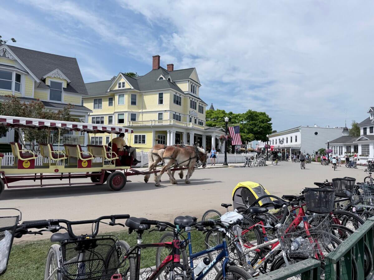 Midwest Weekend Getaway: My Mackinac Island Escape - 4 A horse-drawn carriage passes by yellow buildings and parked bicycles on a sunny day in a quaint town setting.