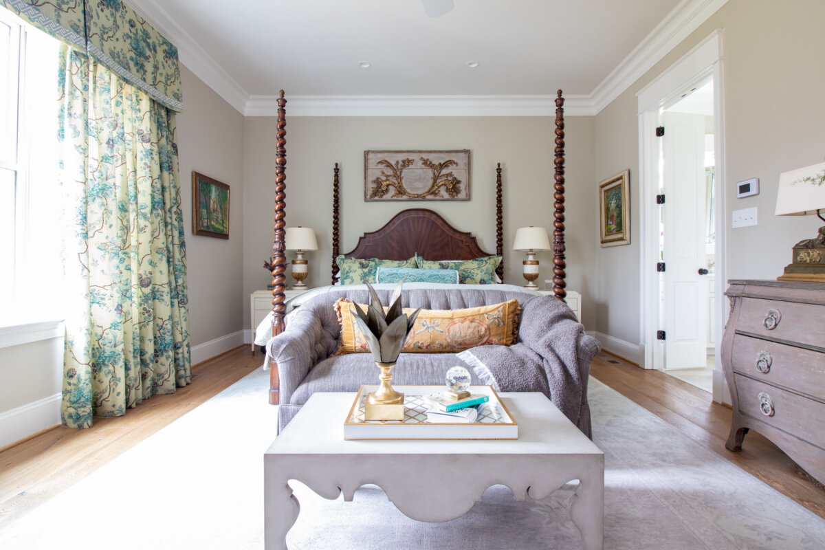 This Designer Wrote the Book on Creating Colorful Spaces — Literally! - 14 A bright, traditional bedroom with a four-poster bed, patterned curtains, a gray sofa, and a coffee table with decorative items and a designer book in front of the bed.