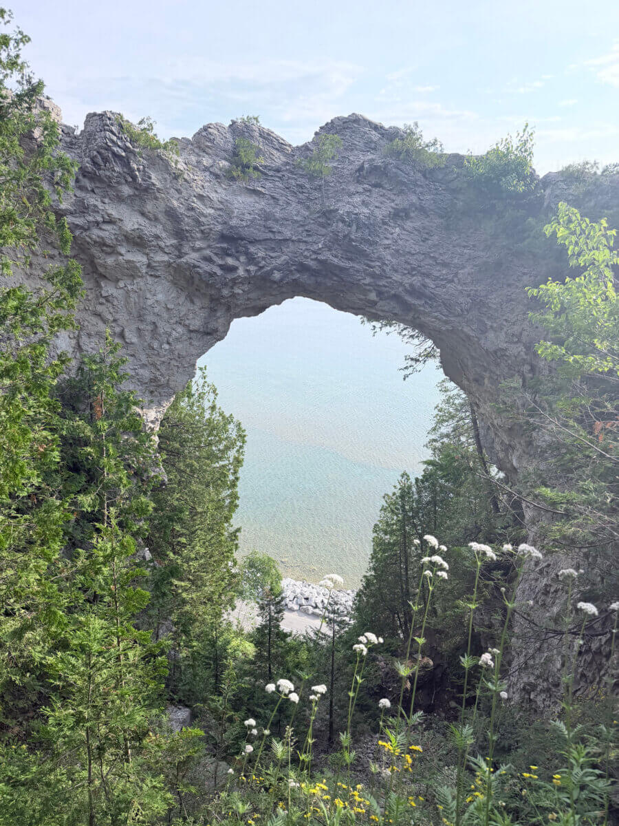 Midwest Weekend Getaway: My Mackinac Island Escape - 7 Natural stone arch rises above clear blue water, framed by green foliage and wildflowers in the foreground.