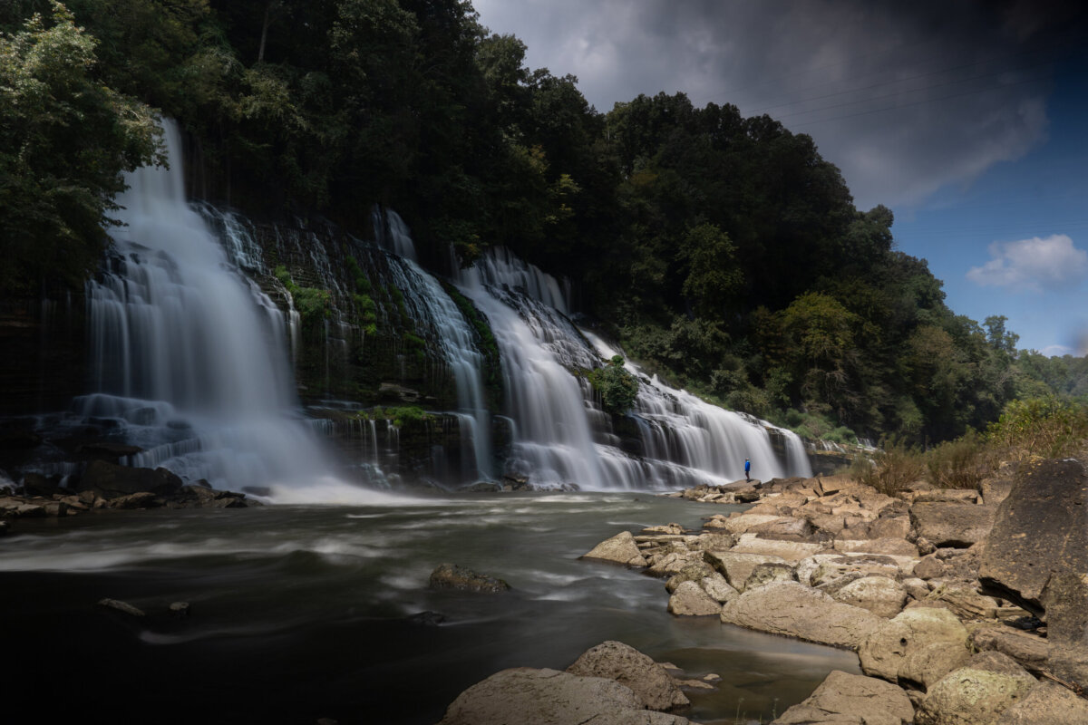 Great Southern Outdoors: Destinations for Active Travelers - 3 A wide waterfall cascades over rocky cliffs surrounded by lush trees, with cloudy skies overhead and rocks in the foregroundβan ideal spot for outdoor adventure vacations.
