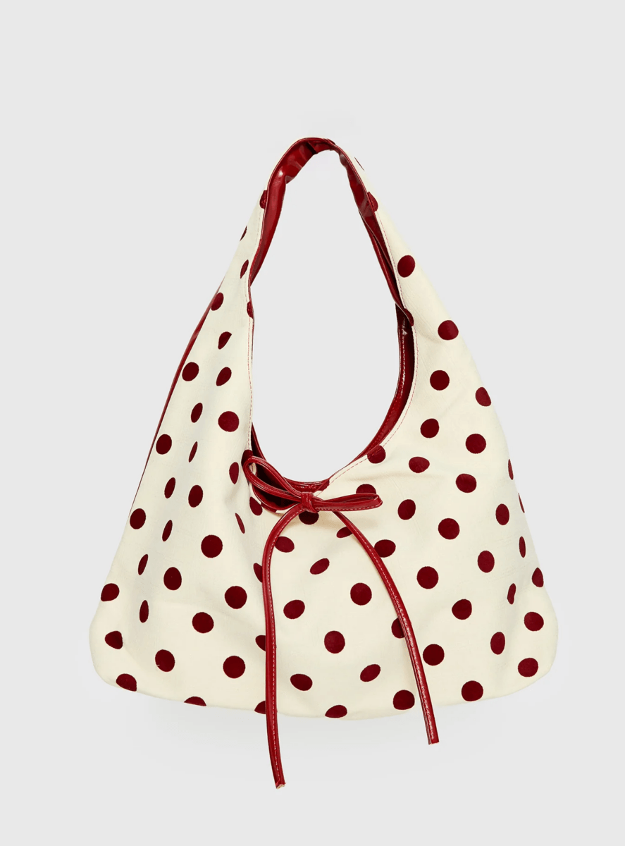 White hobo bag with red polka dots, a red leather handle, and a matching red bow detail on the front—a perfect statement piece for anyone who loves playful polka dot fashion.