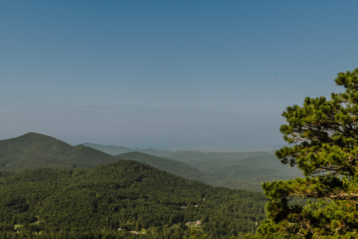 8 Easy Cool-Weather Escapes in the South & Beyond - 5 Green forested hills and distant blue mountains under a clear sky evoke the allure of cool-weather escapes in the South, with pine branches visible on the right side of the imageβperfect for those inspired by travel.
