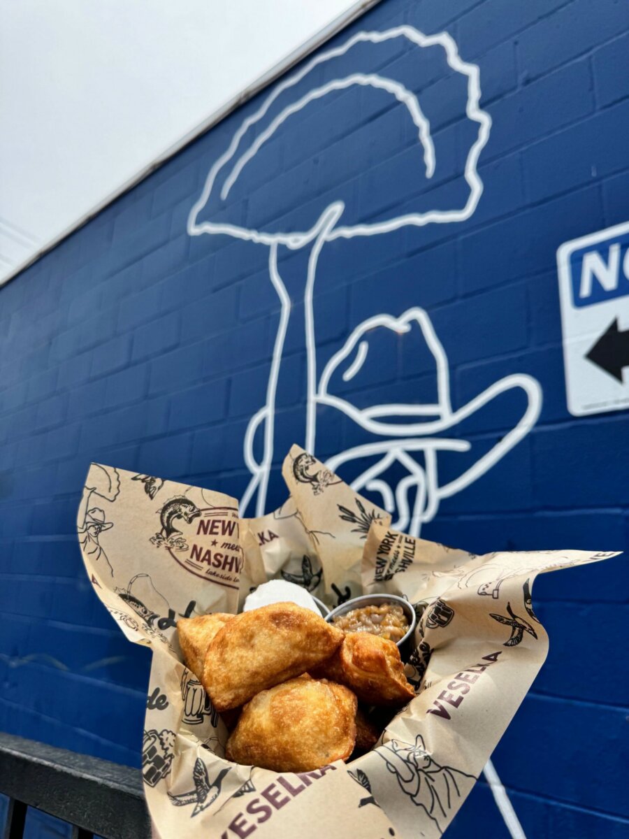 12 New Nashville Restaurants to Try This Month - 16 A basket of fried food with dipping sauce is held in front of a blue mural featuring an outlined figure wearing a hat, capturing the vibrant atmosphere found in many new Nashville restaurants.