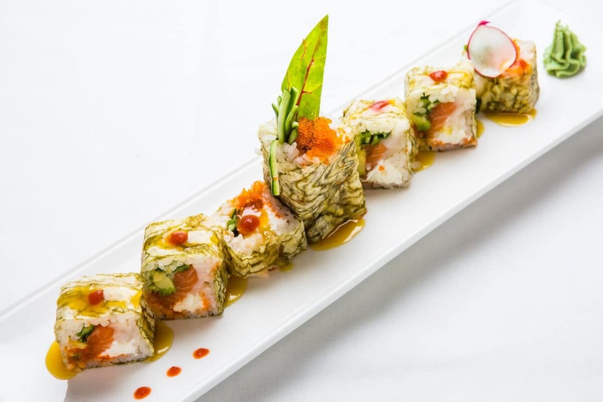 12 New Nashville Restaurants to Try This Month - 15 A rectangular plate from one of the top new Nashville restaurants features six pieces of sushi roll topped with greens, roe, and sauce, arranged diagonally with wasabi and thinly sliced radish garnish on the side.