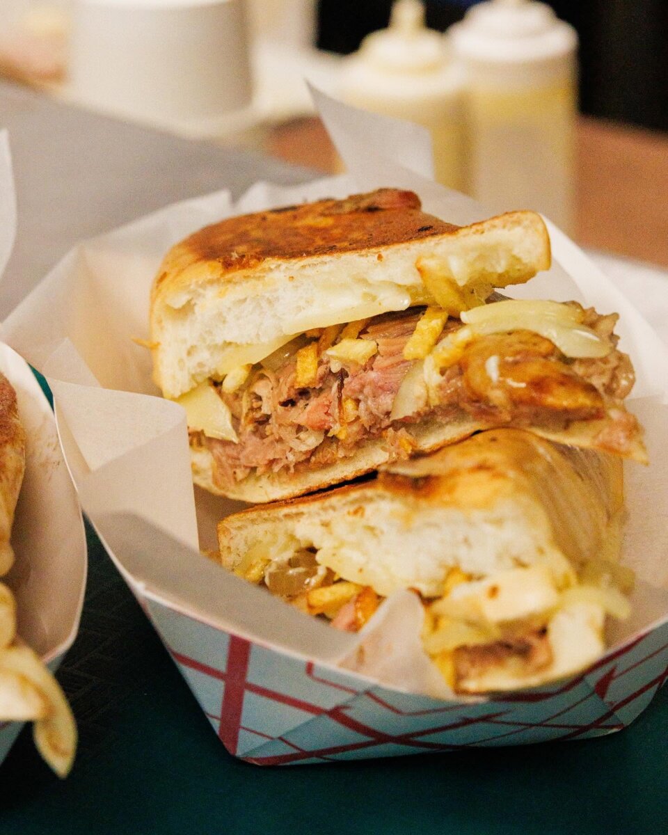 11 Walk-Up Windows To Try in Nashville - 9 A close-up of a sandwich cut in half, filled with shredded meat, fries, cheese, and onions, served in a paper food trayβjust the kind of mouthwatering meal you can find at walk-up windows in Nashville.