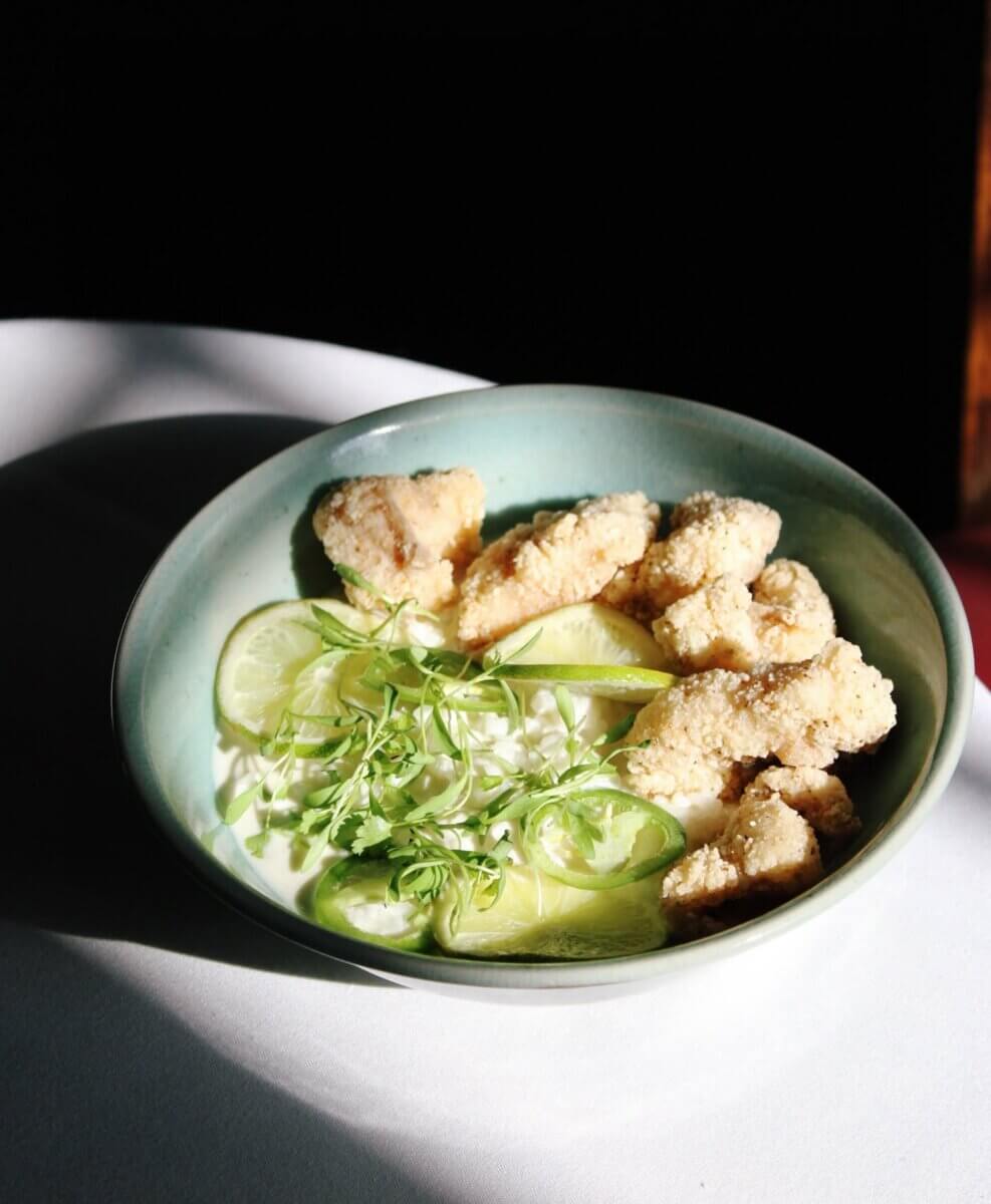 An Ode to Oxford: How to Eat Your Way Through This Delicious Small Town - 8 A bowl of breaded catfish pieces, lime slices, microgreens, and white sauce, served in a green ceramic bowl on a white surface with dramatic lighting.