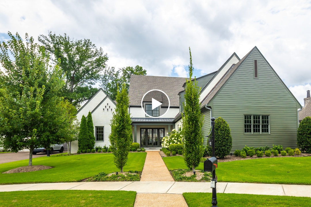 A modern suburban house located at 9071 N Winston Woods Cir, Germantown TN, with green and white siding, manicured lawn, shrubs, and a sidewalk leading to the front door under a cloudy sky.