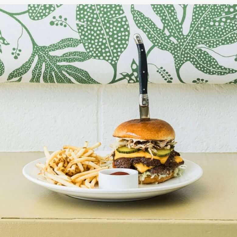 An Ode to Oxford: How to Eat Your Way Through This Delicious Small Town - 10 A double cheeseburger with a knife in the bun is served with a side of thin fries and ketchup on a white plate, set on a beige table.