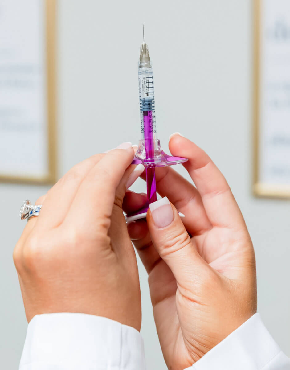 A person holding a syringe filled with purple liquid, preparing for an injection as part of peptide therapy. The background is out of focus.