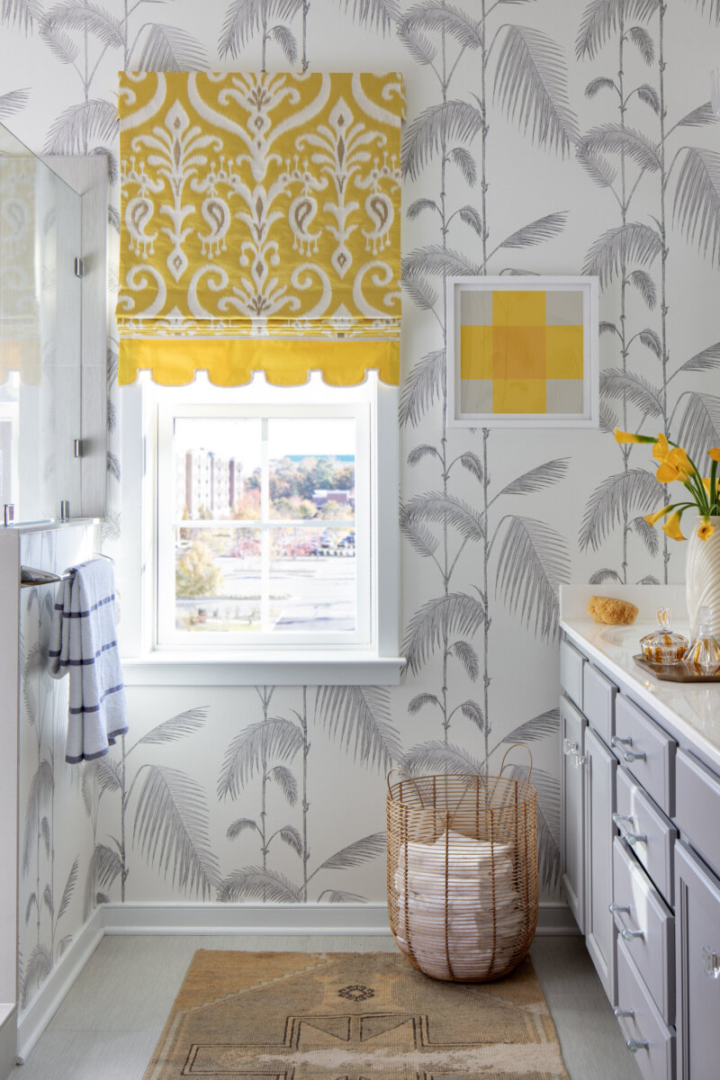 This Designer Wrote the Book on Creating Colorful Spaces — Literally! - 6 Bathroom with palm-patterned wallpaper, a yellow patterned window valance, a wicker laundry basket, and yellow accents on the counter and wall art.