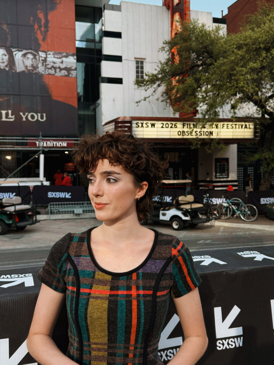 Meet the Memphis Designer Behind the Eerie World of "Obsession" - 7 A person with short, curly hair stands in front of a theater with a marquee reading "SXSW 2026 Film & TV Festival Obsession," at an outdoor SXSW event, where crafted stories and Memphian talent take center stage.