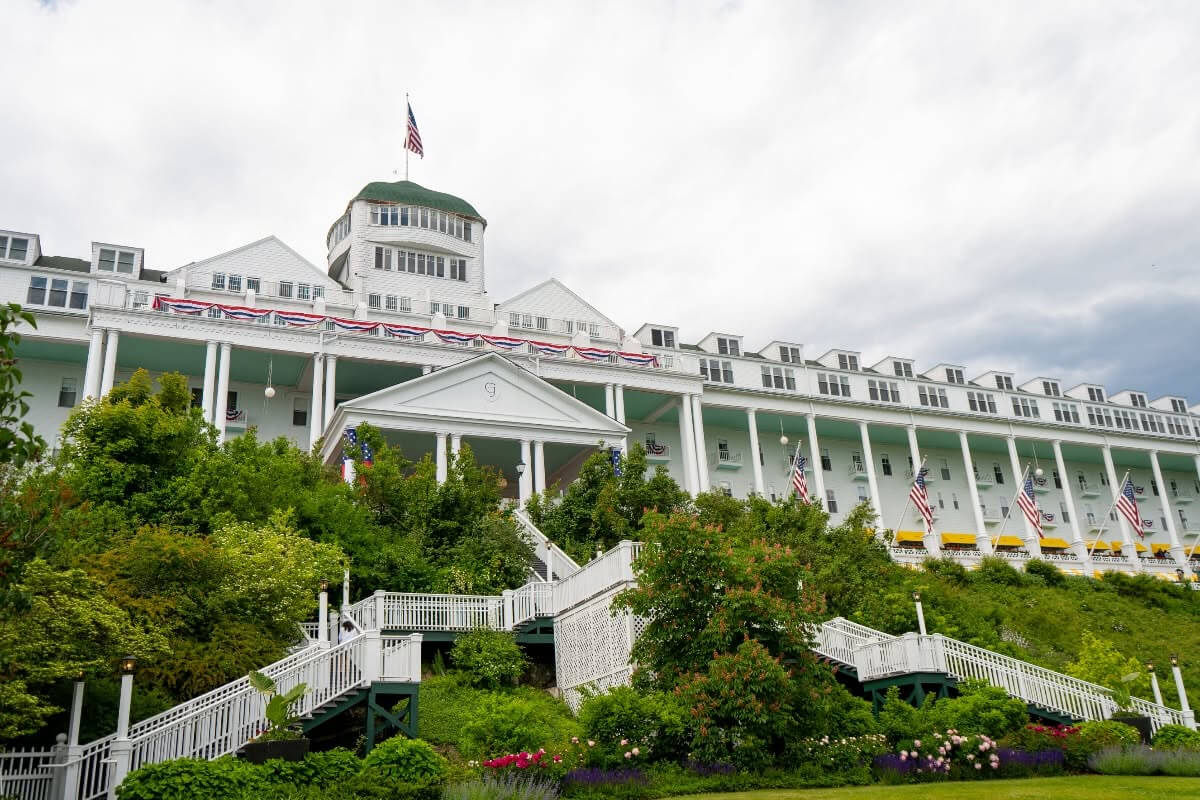 Midwest Weekend Getaway: My Mackinac Island Escape - 6 Large white historic hotel with a green-domed roof, American flags, and a long porch, surrounded by lush greenery and gardens under a cloudy sky—a quintessential Mackinac Island landmark perfect for classic Midwest weekend getaways.