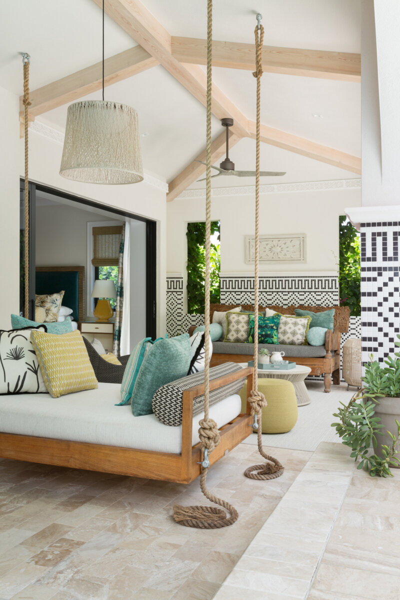 This Designer Wrote the Book on Creating Colorful Spaces — Literally! - 12 Designer outdoor living space featuring a wooden daybed swing, patterned cushions, tiled floor, mosaic wall, ceiling fan, sofa, and large windows opening to greenery.