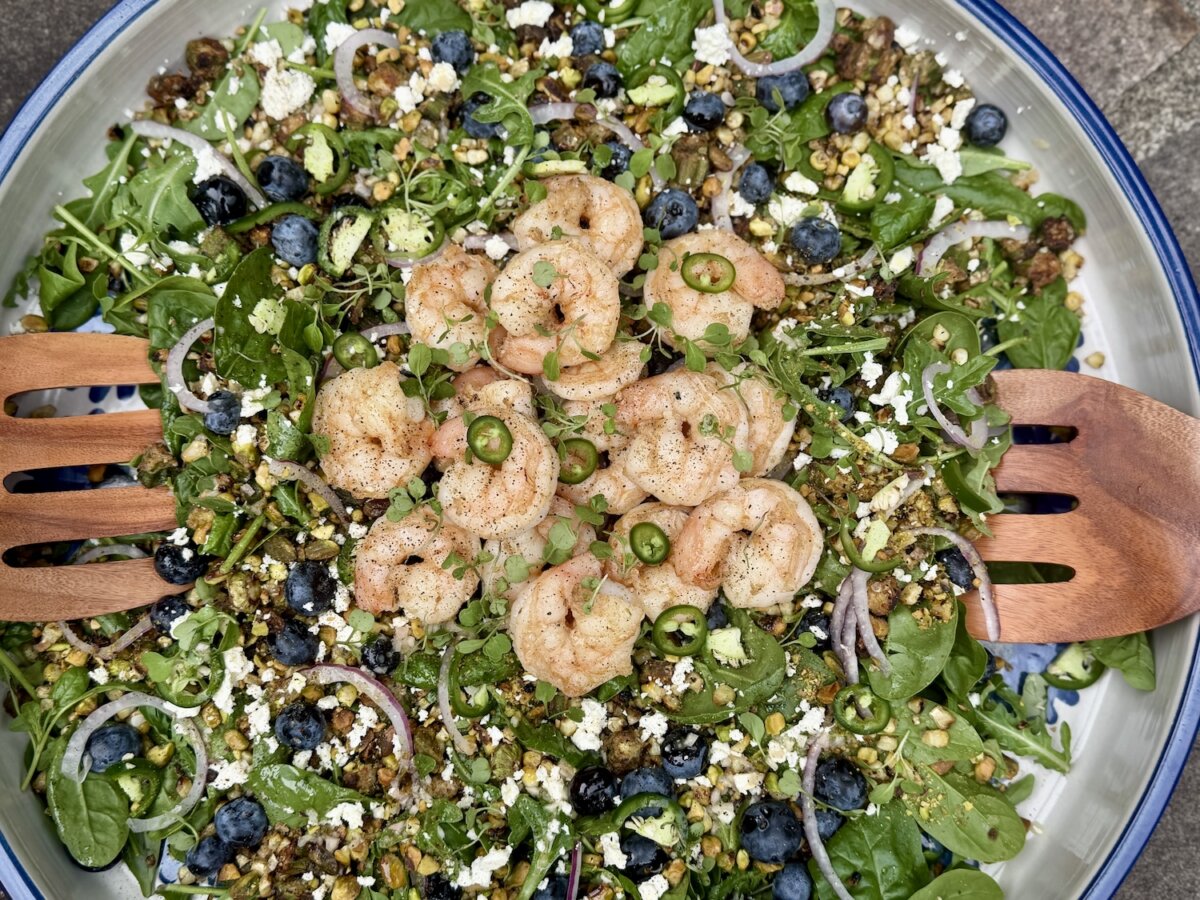 An Unexpected Meal in Jackson, MS, Inspired Our Newest Summer Salad - 4 Enjoy a refreshing summer salad inspired by Jackson MS, featuring shrimp atop fresh greens, blueberries, feta cheese, lentils, sliced jalapeños, and red onions—all beautifully served in a large bowl with wooden salad tongs.