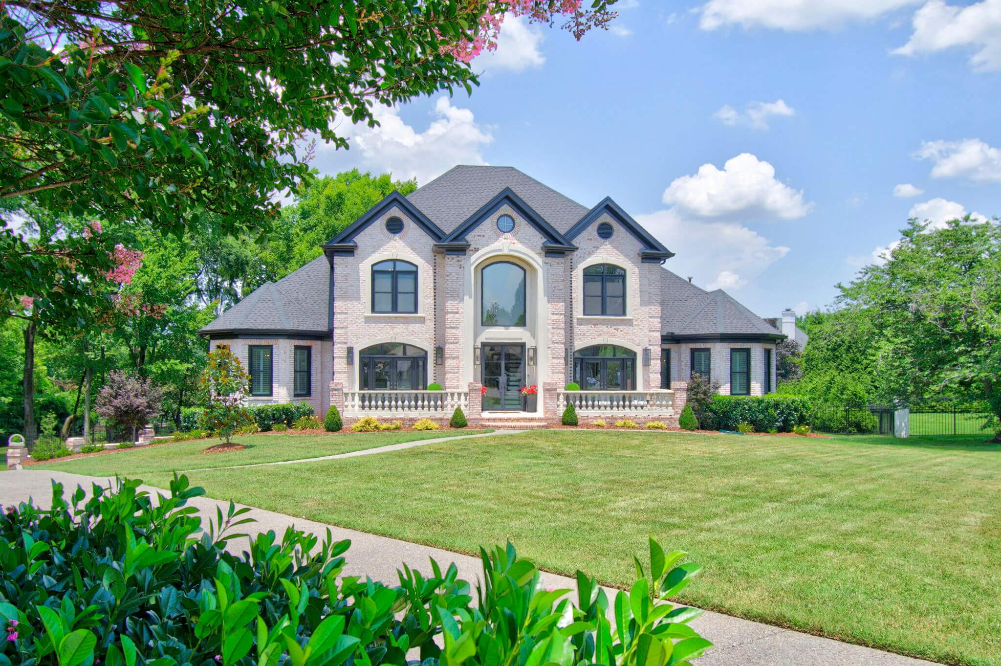 Just Listed! This Renovated Brentwood Home Has a Private Primary Wing, 4 Fireplaces & a Park-Like Backyard - 3 Two-story modern brick house with large windows, manicured lawn, and surrounding trees on a sunny day, located at 9614 Deer Track Court.