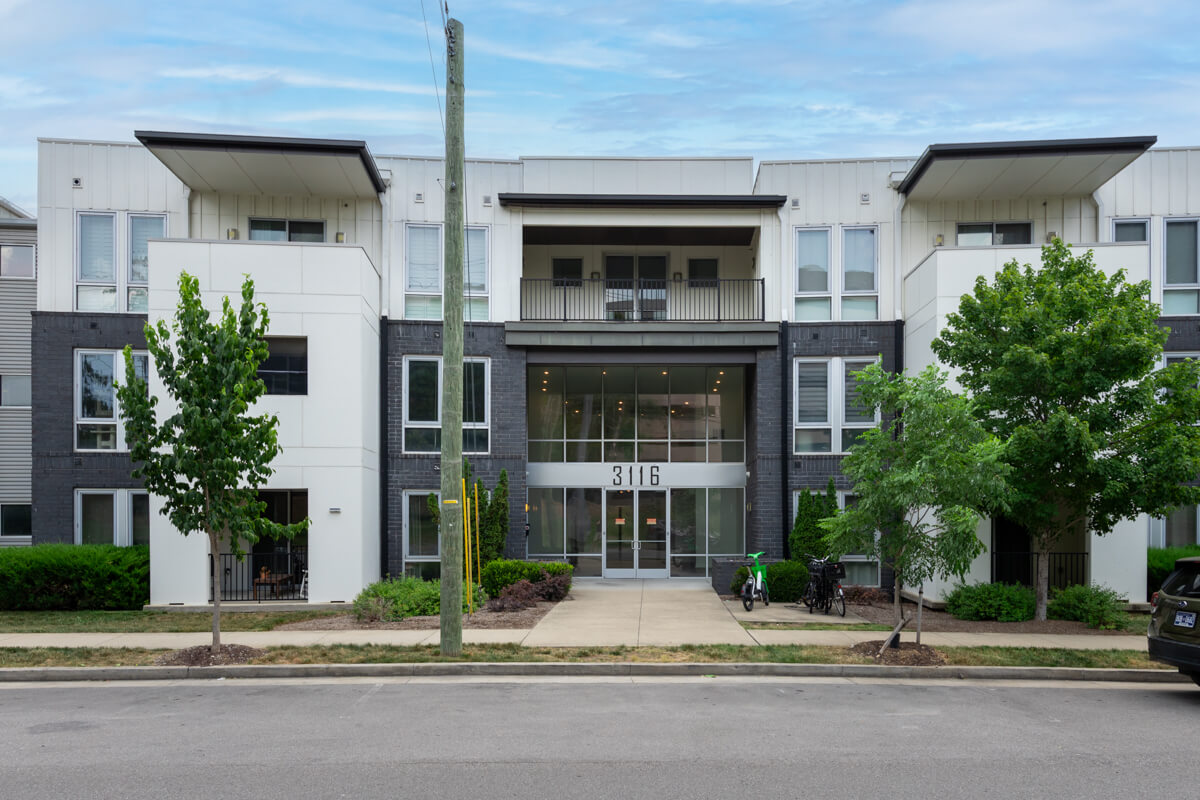 Three-story modern apartment building at 3116 W End Cir, Nashville TN, featuring a central entrance, large windows, balconies, trees, and a sidewalk in front.
