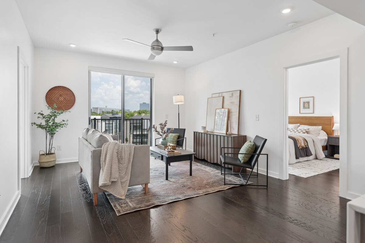 Modern living room at 3116 W End Cir #205, Nashville, with dark wood floors, neutral furniture, and large windows leading to a balcony; a bedroom is visible through an open doorway.