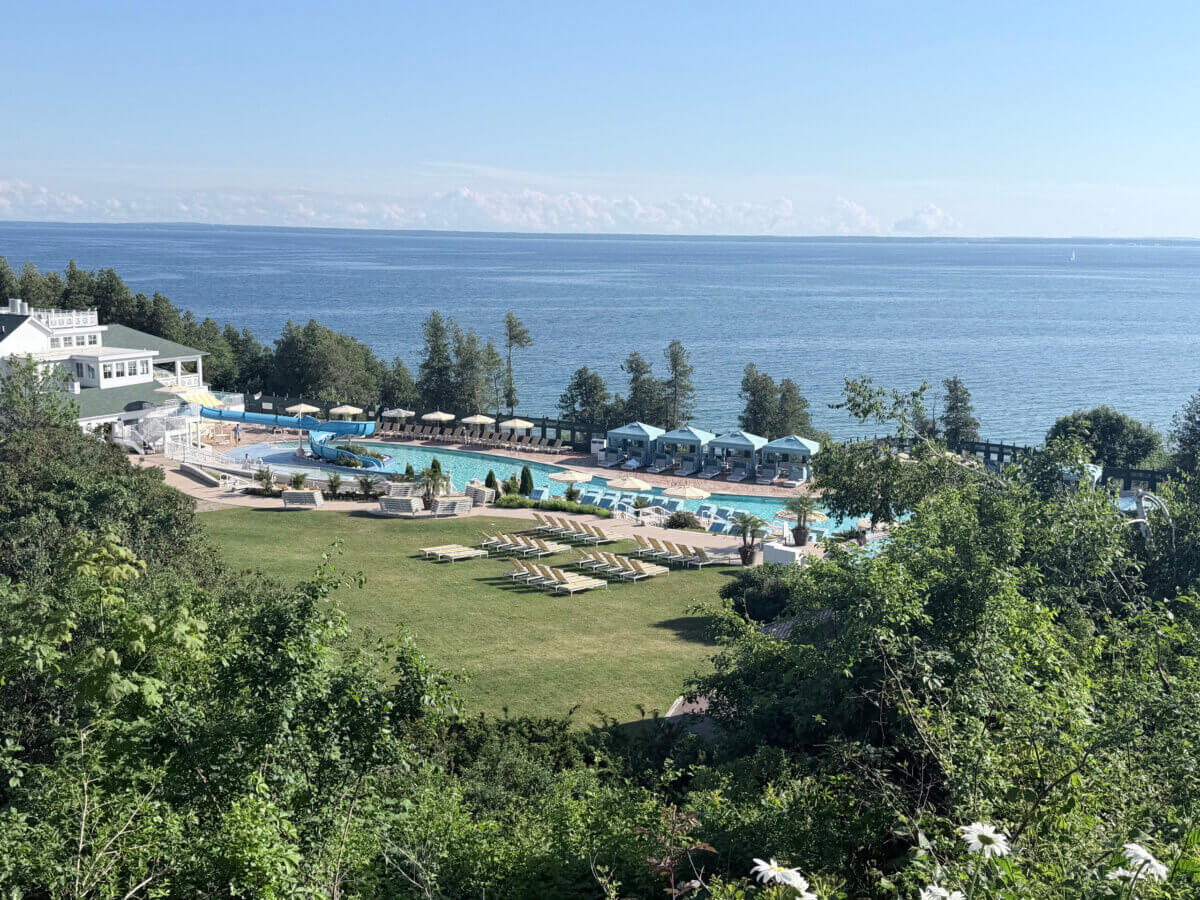 Midwest Weekend Getaway: My Mackinac Island Escape - 15 View of a resort with pools, lounge chairs, and cabanas near a large body of water, surrounded by trees and greenery on a sunny day.