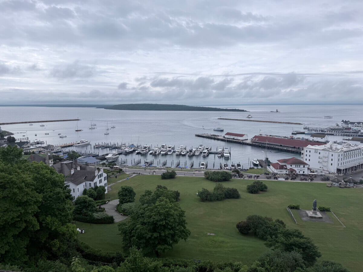 Midwest Weekend Getaway: My Mackinac Island Escape - 2 Overcast view of a marina with boats, docks, and white buildings beside green lawns and trees, overlooking a large body of water.