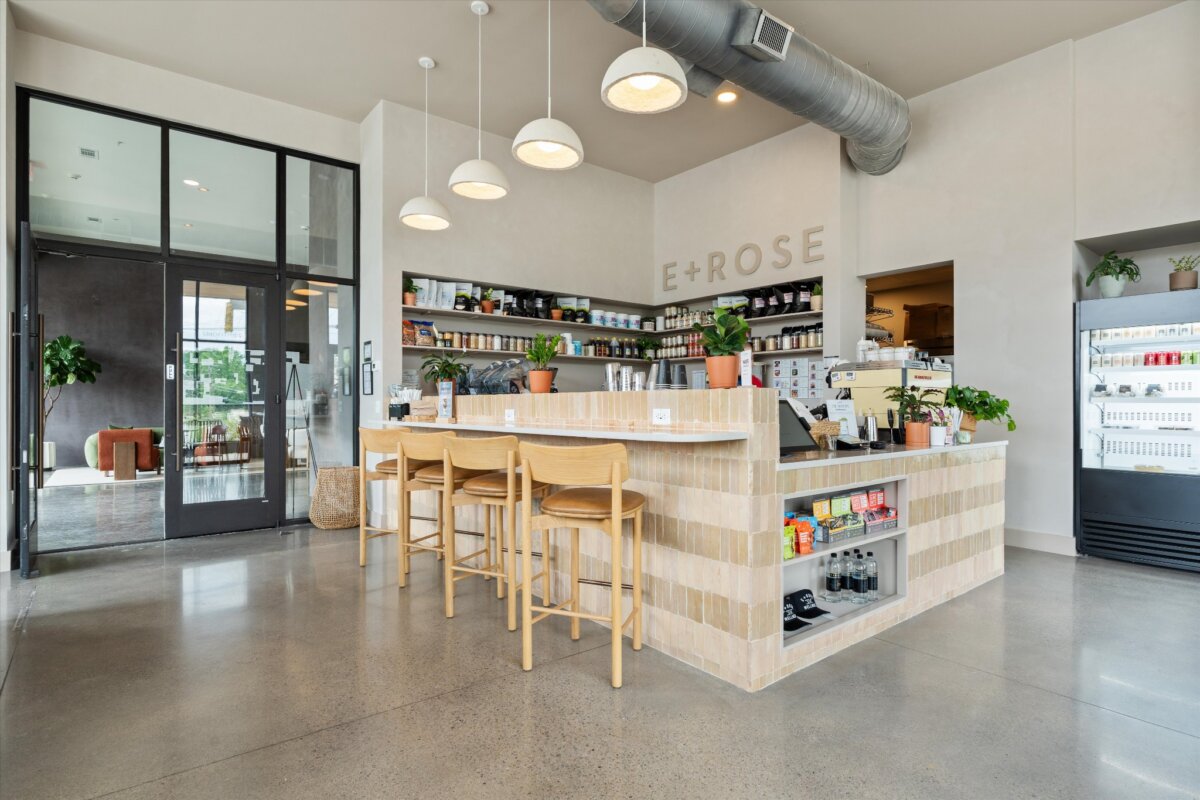 Modern café interior with a tiled counter, wooden stools, hanging lights, plants, and shelves stocked with products. Large glass doors and windows provide natural light, creating an inviting atmosphere at 1090 Haysboro Ave, Nashville.