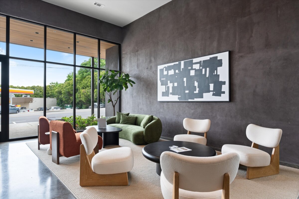 Modern lounge area with white and red chairs, a green sofa, black tables, large window, abstract wall art, and indoor plant at 1090 Haysboro Ave in Nashville, TN.