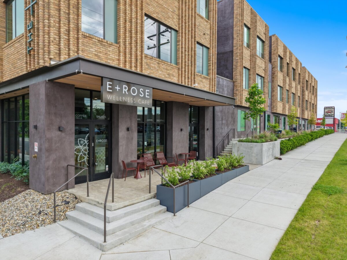 Modern brick wellness cafe with outdoor seating, large windows, and a sign reading “E+ROSE Wellness Cafe” on a city sidewalk with greenery and clear sky, located at 1090 Haysboro Ave in Nashville.