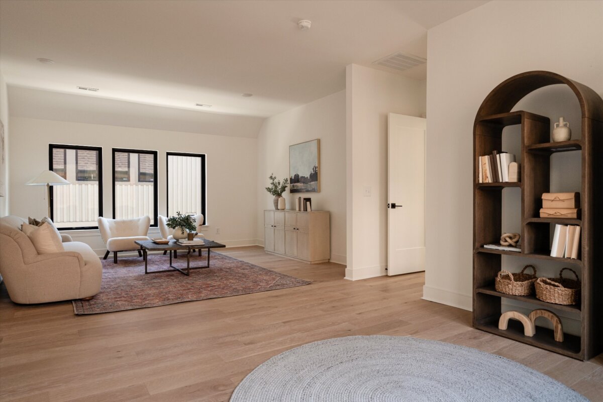 Modern living room with light wood floors, a beige sofa, a round coffee table, a rug, and a dark arched bookshelf—perfectly reflecting the inviting style found at 627 Richmond Bend in Nashville. Three windows and a console cabinet are visible in the background.