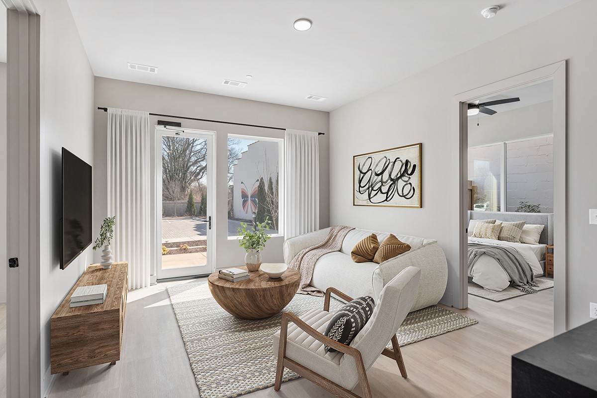 Bright living room with modern decor, a wooden coffee table, TV, and large glass doors leading to a patio at 1090 Haysboro. The bedroom is visible through an open door to the right, highlighting the inviting layout of this charming Nashville home.