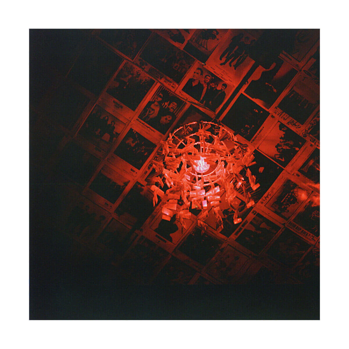 Red light fixture hanging from a ceiling covered with photos or posters, casting a warm glow on the images above.