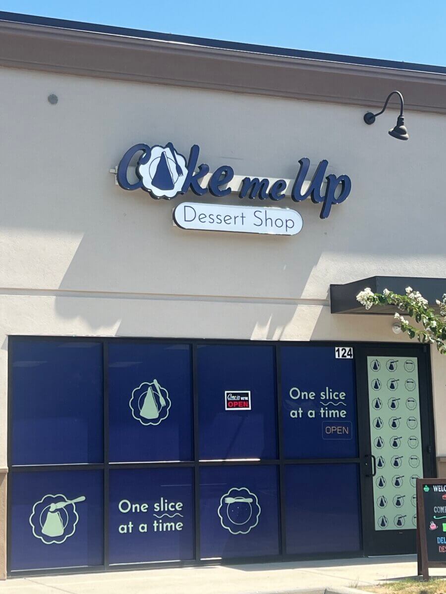 Storefront of “Cake Me Up Dessert Shop,” one of the newest Birmingham restaurants, with blue signage and window decals reading “One slice at a time,” on a sunny day.