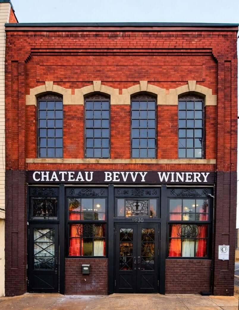 A brick building with large windows and double doors, displaying a sign that reads “CHATEAU BEVVY WINERY” above the entrance, offers an inviting new dining experience inspired by Birmingham restaurants.