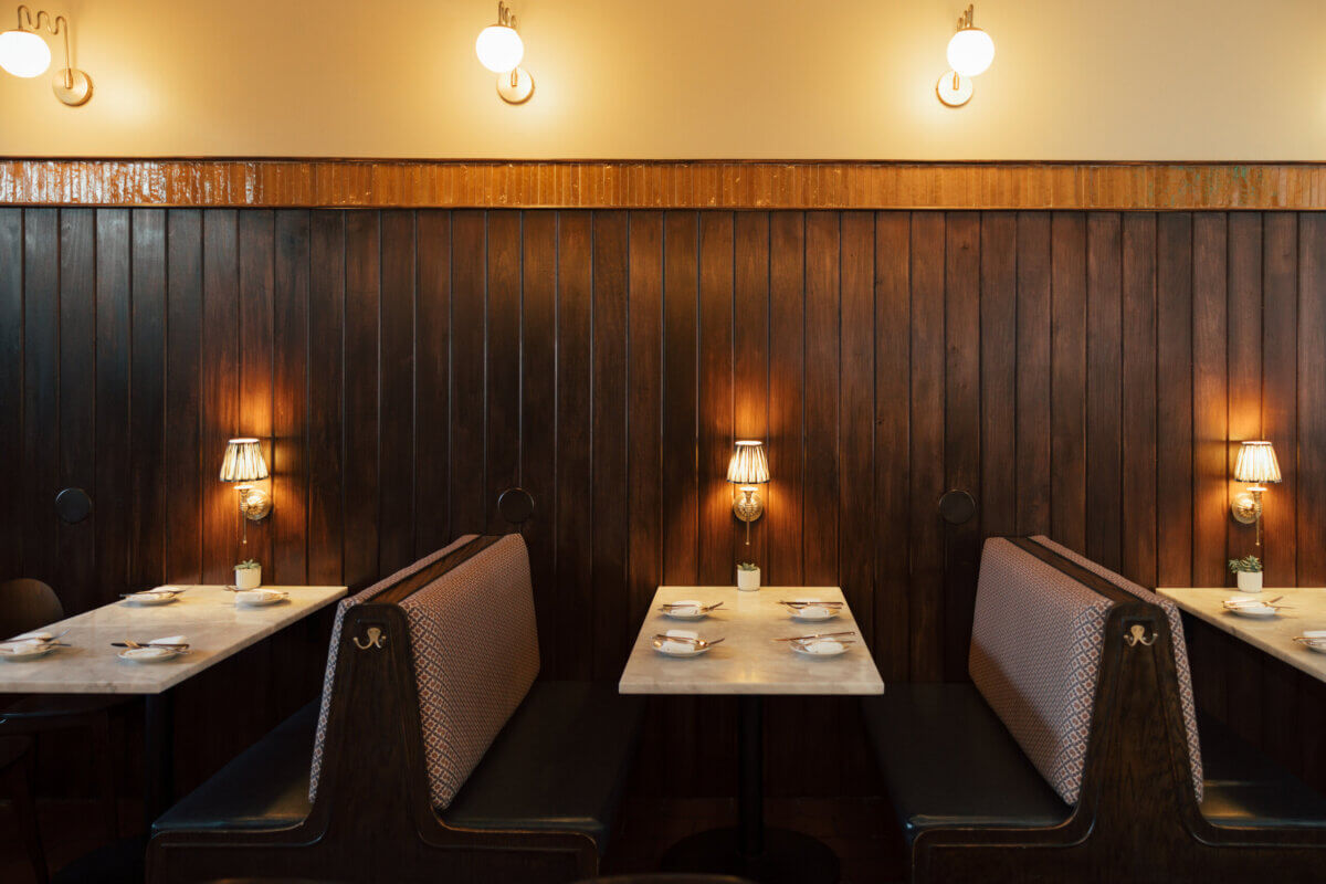 Two empty restaurant booths with marble tables, set with plates and glasses, lit by small lamps against a wooden paneled wall—an essential stop for fall travel and one of the reasons to visit this inviting space.