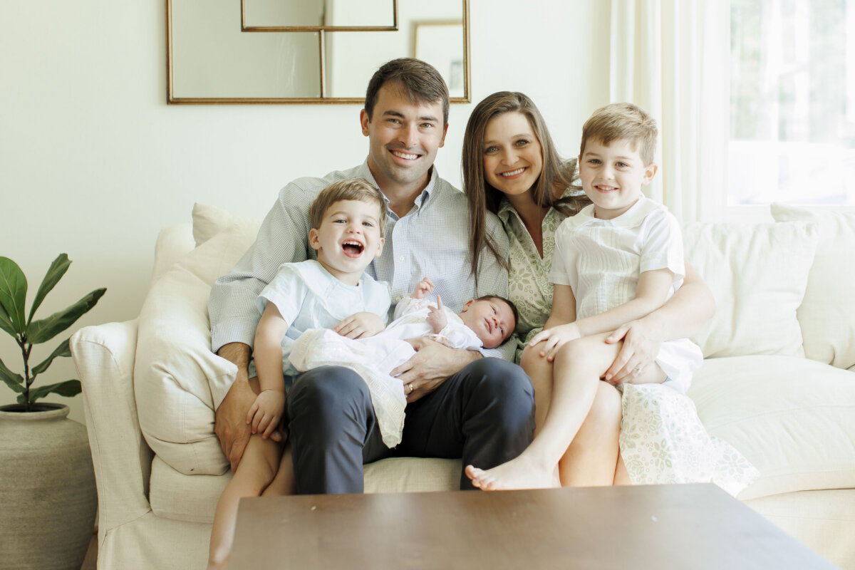 She’s Working to Make Breastfeeding Easier for BHAM Moms - 6 The Clarke family of five sits on a white couch, with the parents in the center, two young boys, and a newborn baby. All are smiling in a bright, softly lit living room.