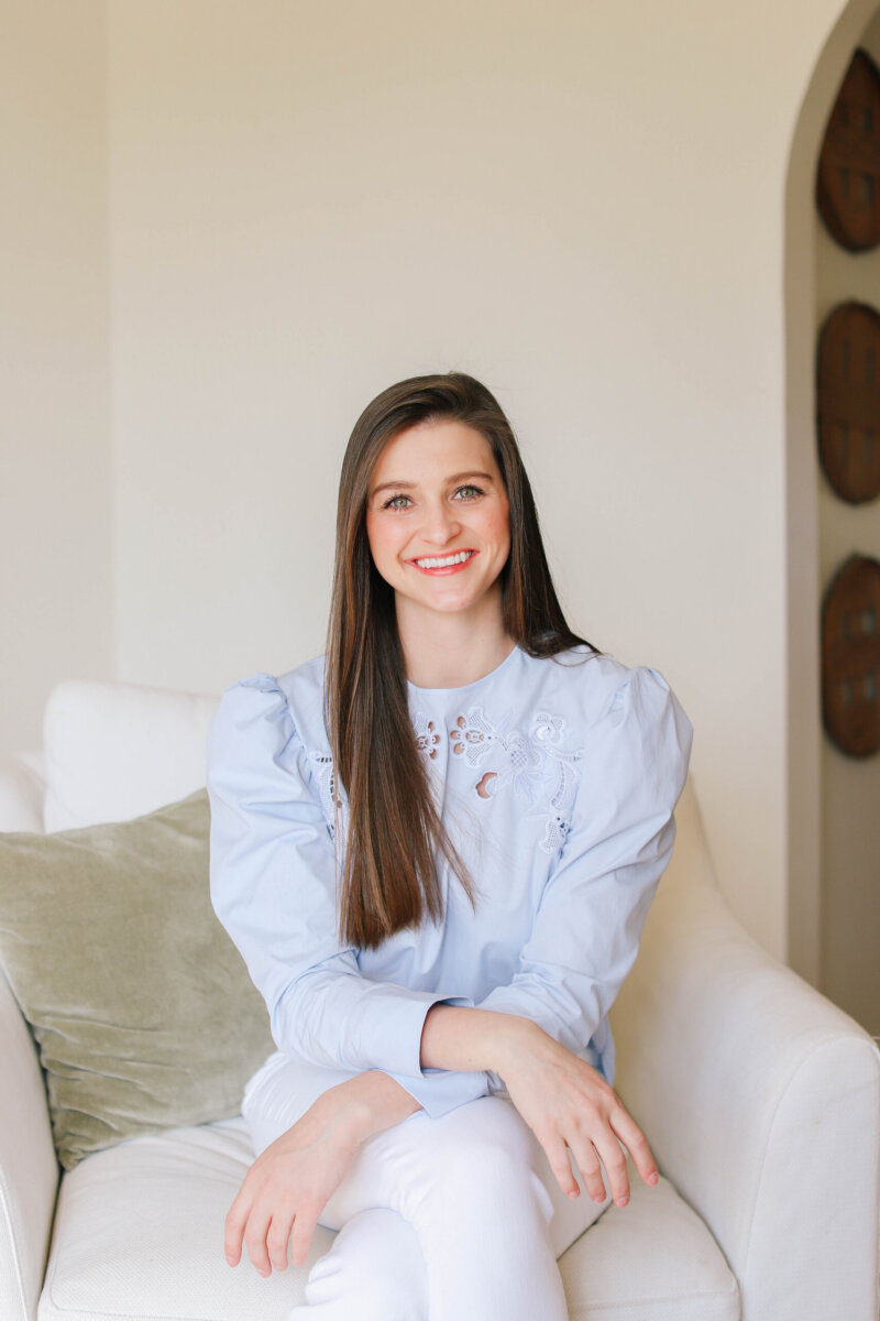 She’s Working to Make Breastfeeding Easier for BHAM Moms - 5 Jordan Clarke with long brown hair sits on a white couch, wearing a light blue blouse and white pants, smiling at the camera.