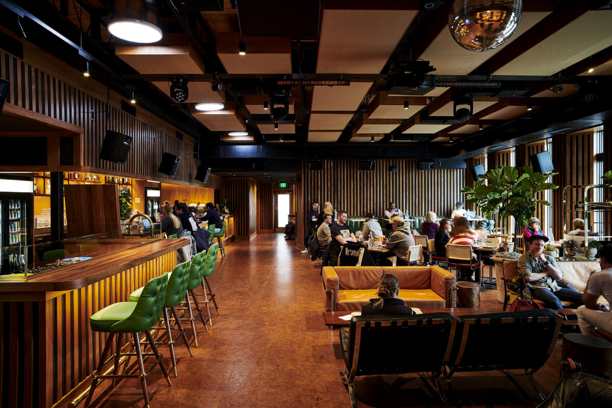 Vinyl, Cocktails & Good Vibes: Birmingham’s New Listening Lounges - 2 Modern bar and lounge inspired by Birmingham’s vibrant nightlife, featuring green barstools, patrons seated at tables and couches, a warm wooden interior, large windows, and a disco ball on the ceiling.
