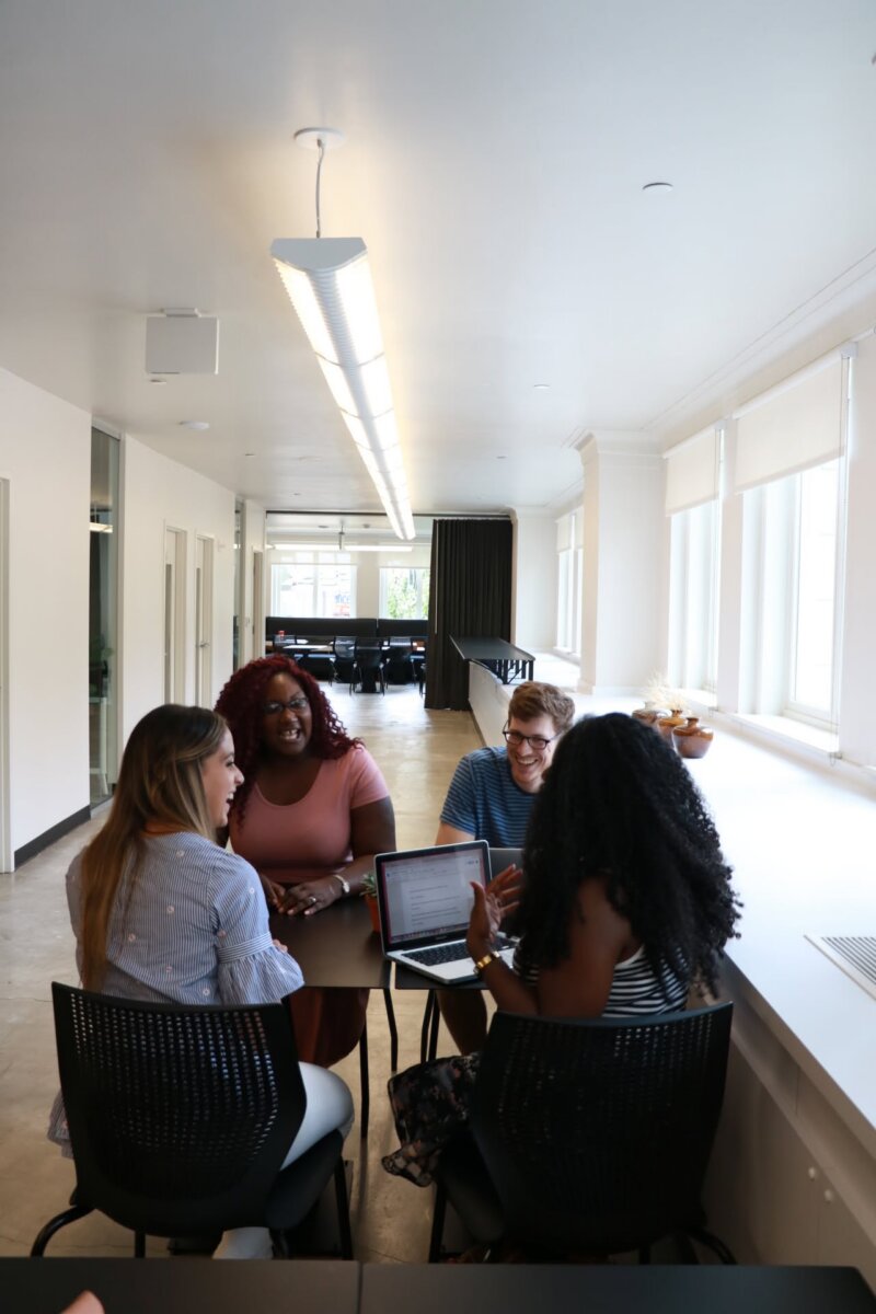 8 Ways to Meet New People in BHAM - 8 Four people sit around a table in a bright office space at Forge, talking and working on a laptop.